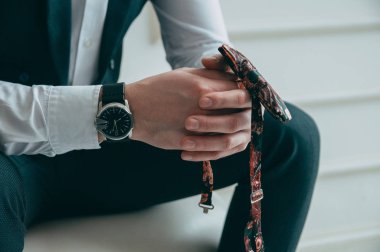 Patronun kırpılmış görüntüsü, el ele tutuşması, kelebeği elinde tutması, pahalı ve şık bir saat, ön manzara. Kavram