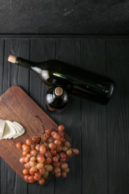 Şişe şarap üzüm ve peynir Camemberg siyah bir ahşap zemin üzerine.