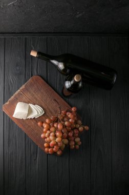 Şişe şarap üzüm ve peynir Camemberg siyah bir ahşap zemin üzerine.