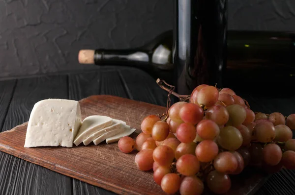 Bottles of wine on a black wooden background with grapes and cheese Camemberg.