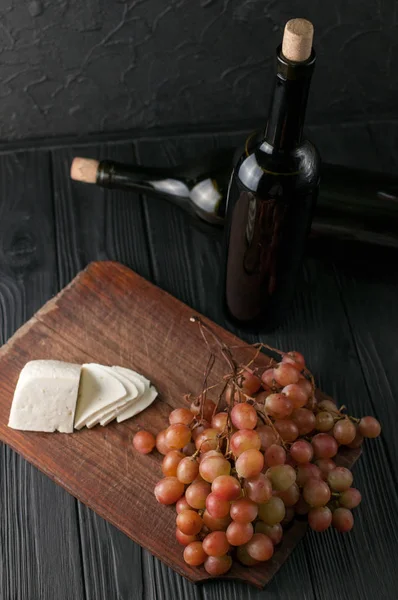 Weinflaschen auf schwarzem Holzgrund mit Trauben und Käse-Camemberg. — Stockfoto