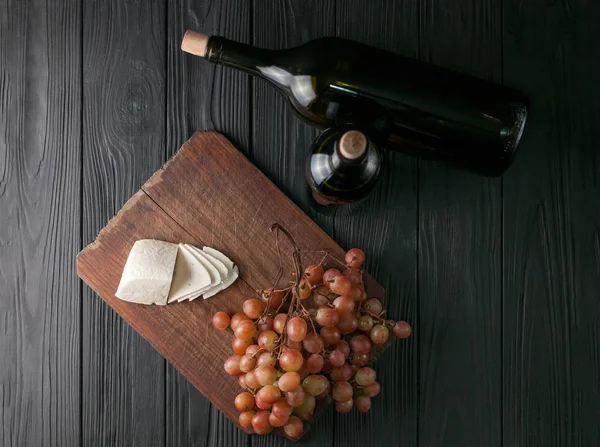 Weinflaschen auf schwarzem Holzgrund mit Trauben und Käse-Camemberg. — Stockfoto