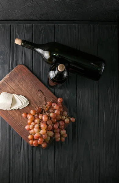 Weinflaschen auf schwarzem Holzgrund mit Trauben und Käse-Camemberg. — Stockfoto