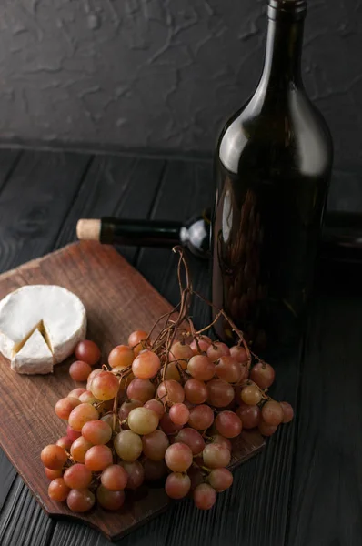 Bottles of wine on a black wooden background with grapes and cheese Camemberg