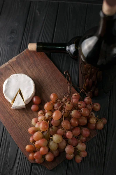 Weinflaschen Auf Schwarzem Holzgrund Mit Trauben Und Käse Camemberg — Stockfoto