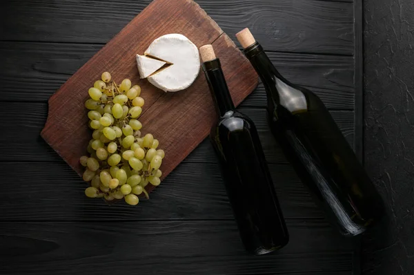 Bottles of wine on a black wooden background with grapes and cheese Camemberg