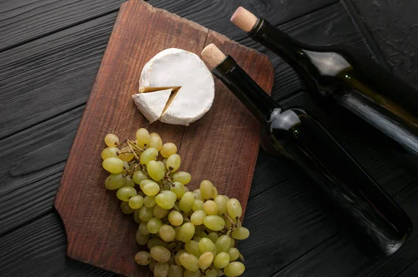 Garrafas de vinho sobre fundo de madeira preta com uvas e queijo Camemberg . — Fotografia de Stock