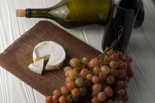 Garrafas de vinho sobre fundo branco de madeira com uvas e queijo Camembert . — Fotografia de Stock