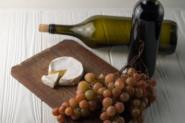 Garrafas de vinho sobre fundo branco de madeira com uvas e queijo Camembert . — Fotografia de Stock