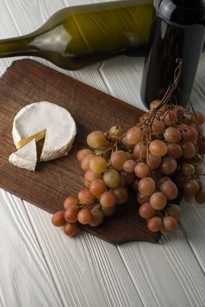 Garrafas de vinho sobre fundo branco de madeira com uvas e queijo Camembert . — Fotografia de Stock