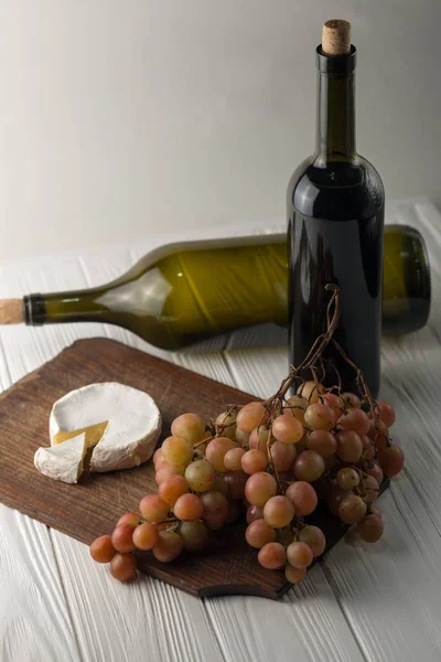 Weinflaschen auf weißem Holzgrund mit Trauben und Camembert. — Stockfoto