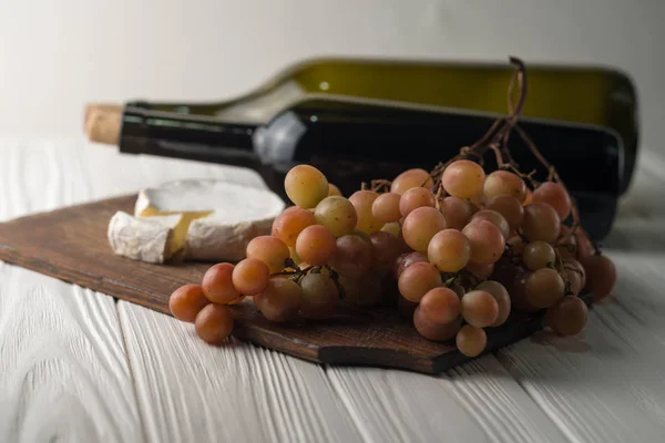 Weinflaschen auf weißem Holzgrund mit Trauben und Camembert. — Stockfoto