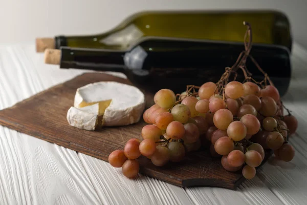 Garrafas de vinho sobre fundo branco de madeira com uvas e queijo Camembert . — Fotografia de Stock