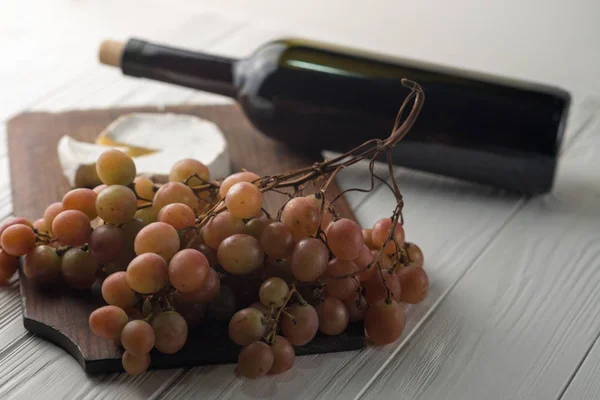 Weinflaschen auf weißem Holzgrund mit Trauben und Camembert. — Stockfoto