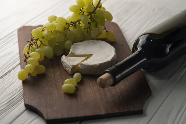 Weinflaschen auf weißem Holzgrund mit Trauben und Camembert. — Stockfoto