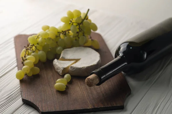 Weinflaschen auf weißem Holzgrund mit Trauben und Camembert. — Stockfoto