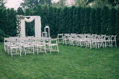 Beautiful wedding set up. Area of the wedding ceremony. Round arch, white chairs decorated with flowers, greenery. Cute, trendy rustic decor. Part of the festive decor, floral arrangement. clipart