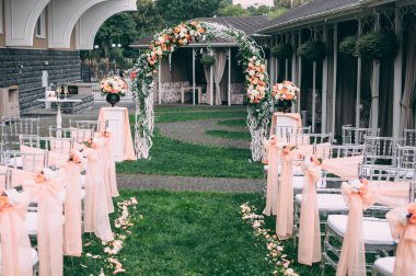 Güzel bir düğün hazırlığı. Düğün merasiminin alanı. Yuvarlak kemer, çiçeklerle süslenmiş beyaz sandalyeler, yeşillik. Sevimli, modaya uygun kırsal dekor. Festival dekorunun bir parçası, çiçek aranjmanı..