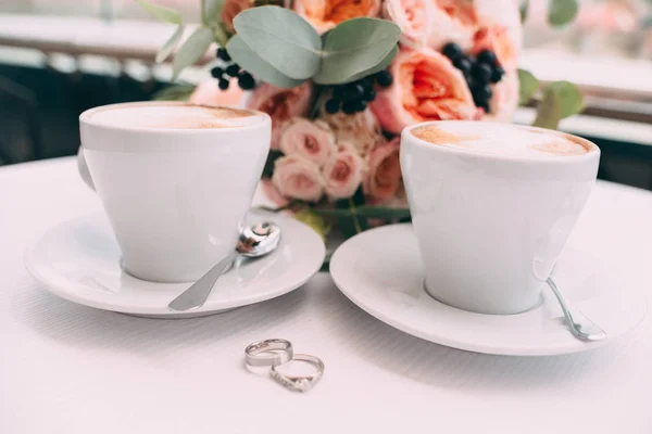 Βέρες σε λευκό πίνακα στο φόντο του μια γαμήλια ανθοδέσμη και δύο φλιτζάνια καφέ — Φωτογραφία Αρχείου