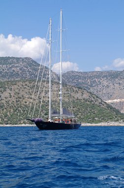 Dağların arka plan üzerinde denizde siyah bir gövde ile yelkenli