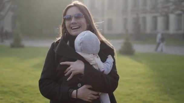 Una joven y hermosa madre bailando con un niño pequeño sentado en un portabebés frente a un viejo castillo — Vídeos de Stock