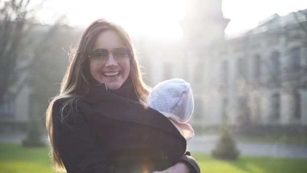 A young beautiful woman whirling back and forth, jumping with her yearling daughter in a baby sling in front of an old castle — Stock Video