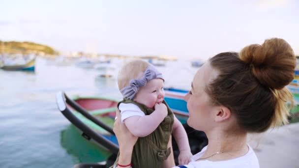 Een jonge moeder kussen haar jaarling baby tweemaal in de kleine neus in de buurt van de zee — Stockvideo