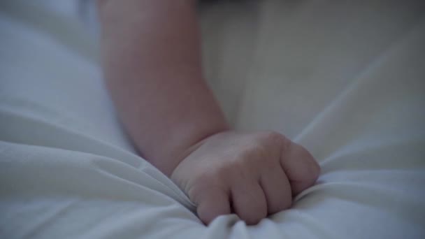 一个特写镜头计划, 一个小婴儿穿着花礼服躺在白色封面上的肚子上, 试图慢动作站起来 — 图库视频影像