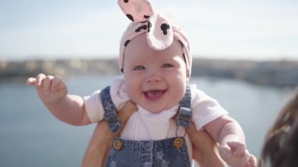 A close-up plan of a squinting from the sun baby and smiling to mother — Stock Video