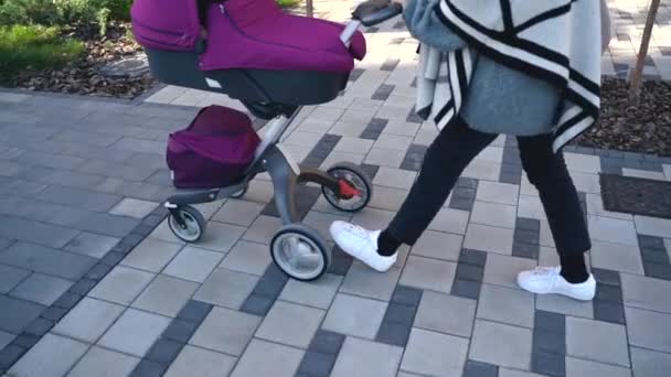 Ein mittlerer Plan von Frauenbeinen in weißen Schuhen, die mit einem Kinderwagen in Zeitlupe auf dem Bürgersteig gehen — Stockvideo