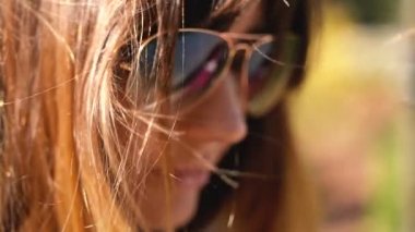 Güneş gözlüğü kadının yüzüne yakın çekim planı. Güneşte parıldayan ve yavaş hareket rüzgarda sallayarak kahverengi incecik doğal kadının saç