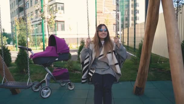 Середній план жінки, що їде на гойдалці у повільному темпі, португальська дитяча коляска поруч . — стокове відео