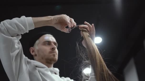 Een middelste plan van een mannelijke kapper een lok van blonde haren knippen — Stockvideo