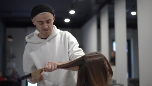 Un peluquero masculino peina y corta un cabello castaño desbordante — Vídeo de stock