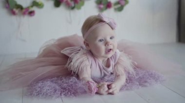 Mor kapak yüzüstü yatarken ve elinde bir gül pembe elbiseli küçük bir bebek photosession
