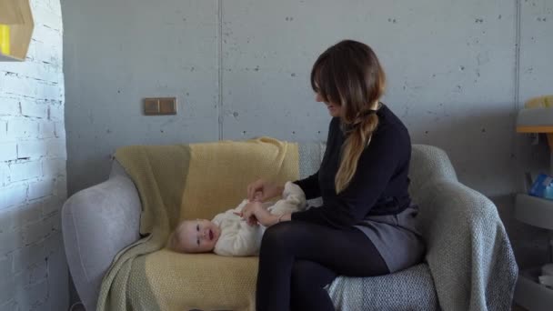 Eine junge schöne Mutter spielt mit ihrem fünf Monate alten Baby auf einem Sofa im Wohnzimmer — Stockvideo