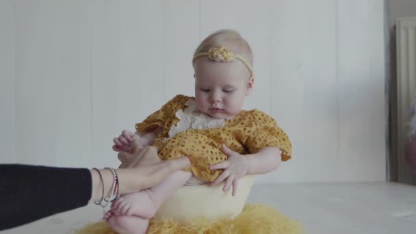 Una niña con un vestido amarillo y una banda de pelo amarillo florecido está sentada en una cáscara de huevo como una chica — Vídeo de stock