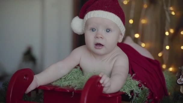 Un petit bébé allongé sur le traîneau du Père Noël dans un chapeau et un costume de Noël, séance photo du Nouvel An — Video