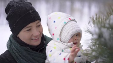 Bir anne ve bir kış parkta köknar ağacı dokunmaktan ve gülümseyen bir bebek yakın çekim bir planı