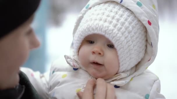 План крупным планом молодой матери, держащей своего новорожденного ребенка в белой теплой шляпе в зимнем парке — стоковое видео