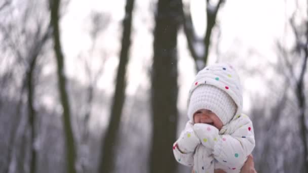 A young woman toss up the baby in a white warm suit in the winter park — Stock Video