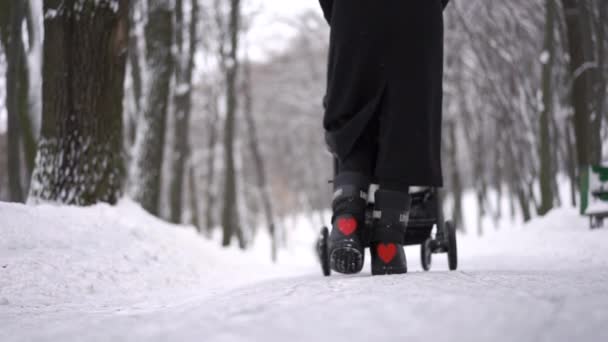Вид ззаду жінки, що йде з дитячим коляскою в зимовому лісі в повільному русі — стокове відео