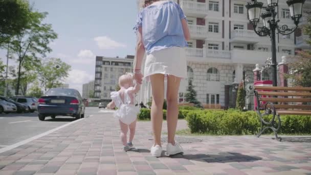 Een klein meisje in witte jurk wandelingen met haar moeder en valt — Stockvideo