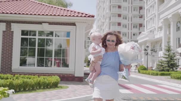 A mother goes through the street with a baby and flowers — Stock Video