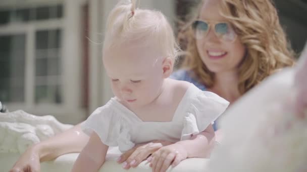 Ένα μωρό σε ένα λευκό φόρεμα παίζει στο σιντριβάνι με σταγόνες σε ραμίδη — Αρχείο Βίντεο