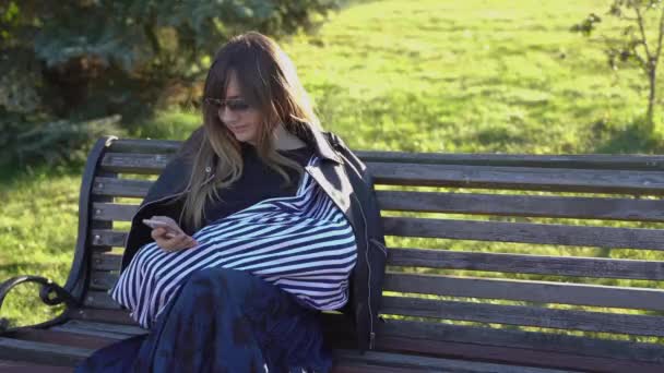 Μια νεαρή γυναίκα με το μαύρο μπουφάν θηλάζει το μωρό της στο πάρκο σε 4K — Αρχείο Βίντεο