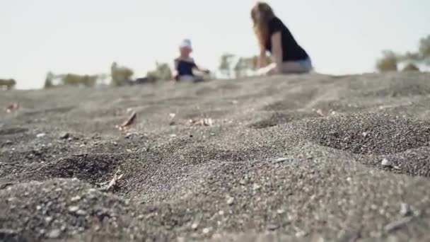 Een klein meisje met haar moeder zitten op de zwarte vulkanische zandstrand — Stockvideo