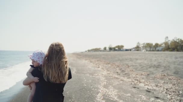 Una joven camina por la costa del mar con su bebé en las manos — Vídeos de Stock