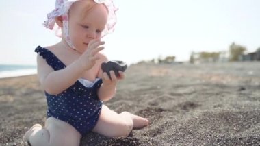 Bir bebek volkanik kum sahilde siyah taş dikkatle bakar