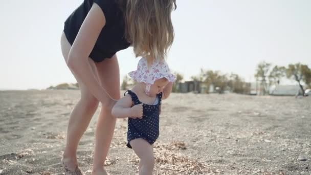 Una niña intenta dar sus primeros pasos en la playa de arena volcánica de Santorini — Vídeo de stock